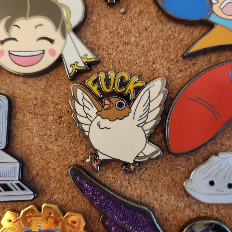 Close-up of a metallic pin of a small bird throwing its wings up and screaming "FUCK"