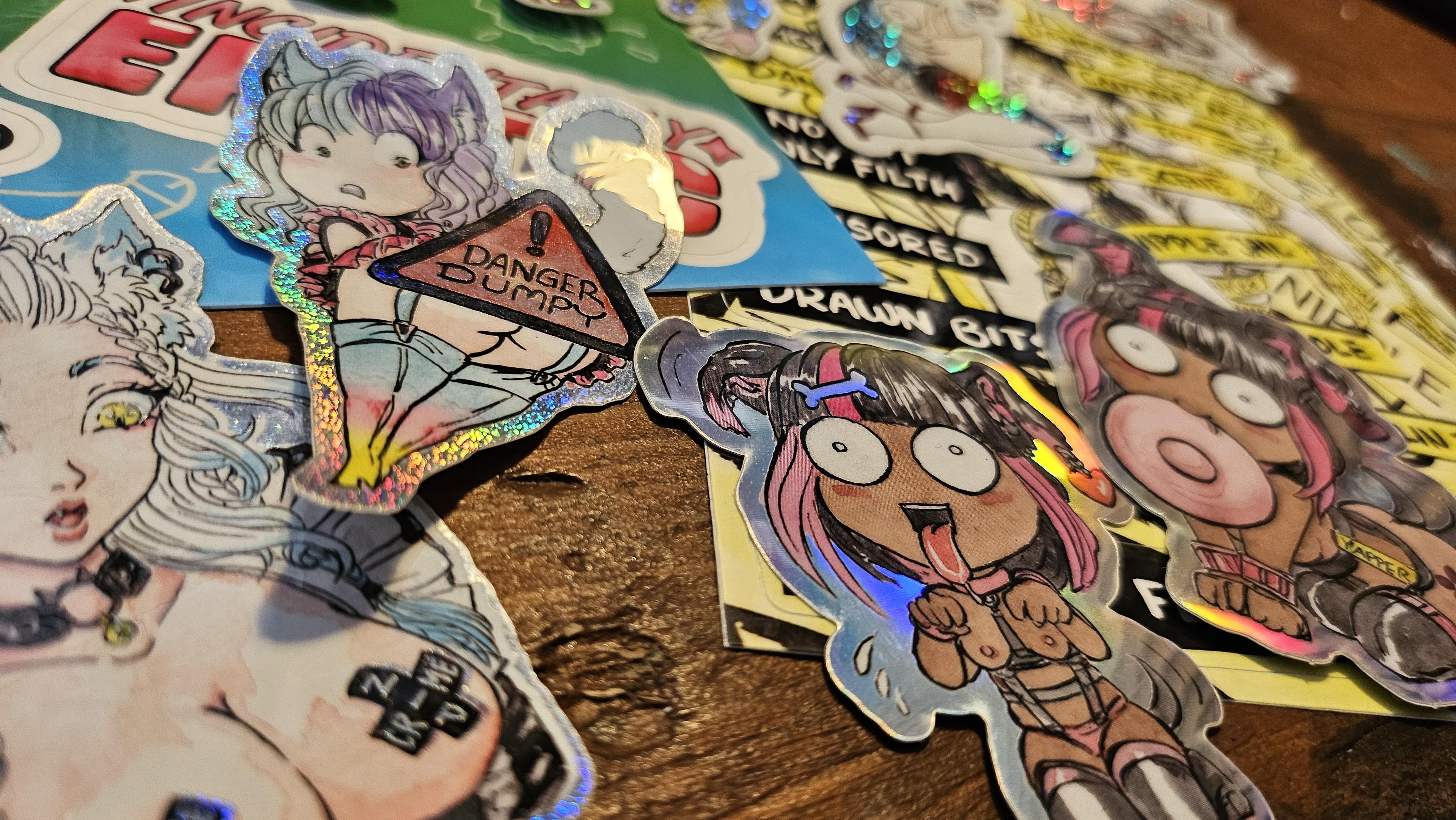 Angled shot of a bunch of colourful stickers laid out on a desk. They all have a theme of anti-censorship and cute titties and butts.