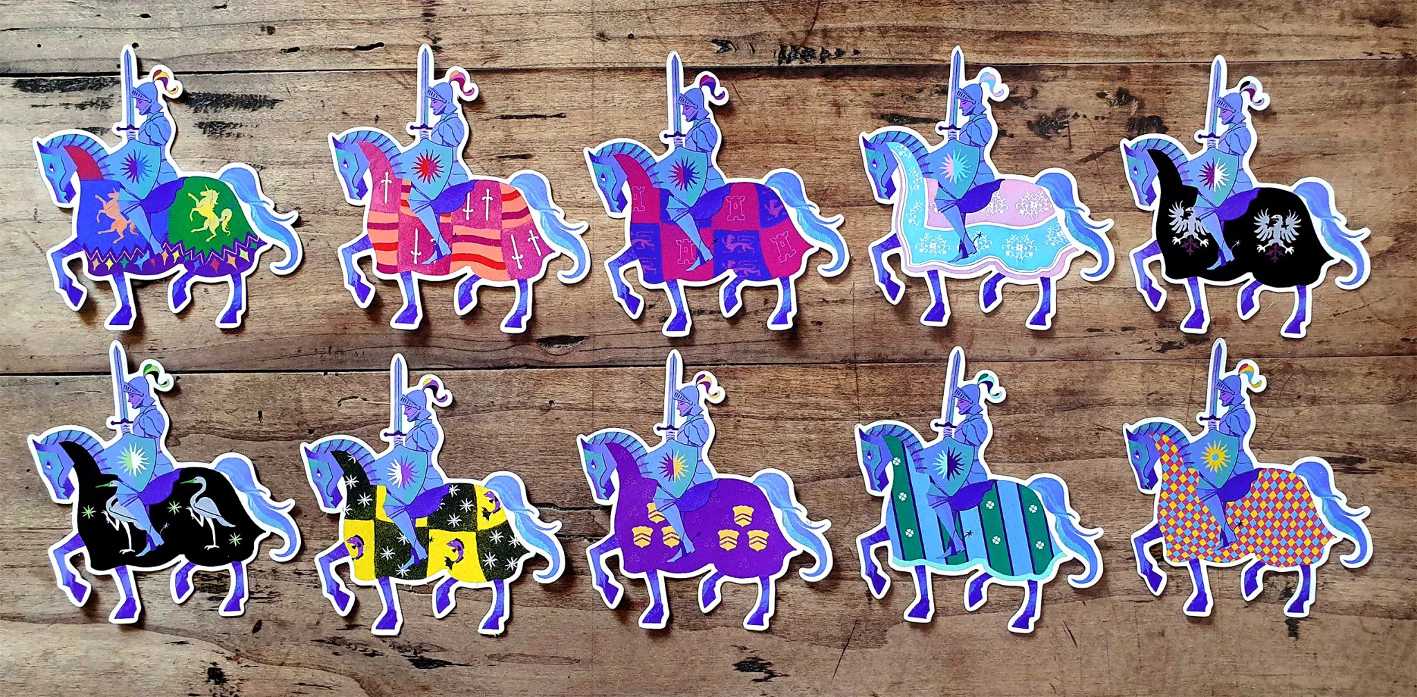 photo of 10 stickers laid out on a wood table featuring knights on horses
the illustration always features a knight on their steed, but the colours of the caparison change based on the flag they represent. In order: Rainbow pride, lesbian, bi, trans, asexual, aromantic, non-binary, intersex, gay, pan