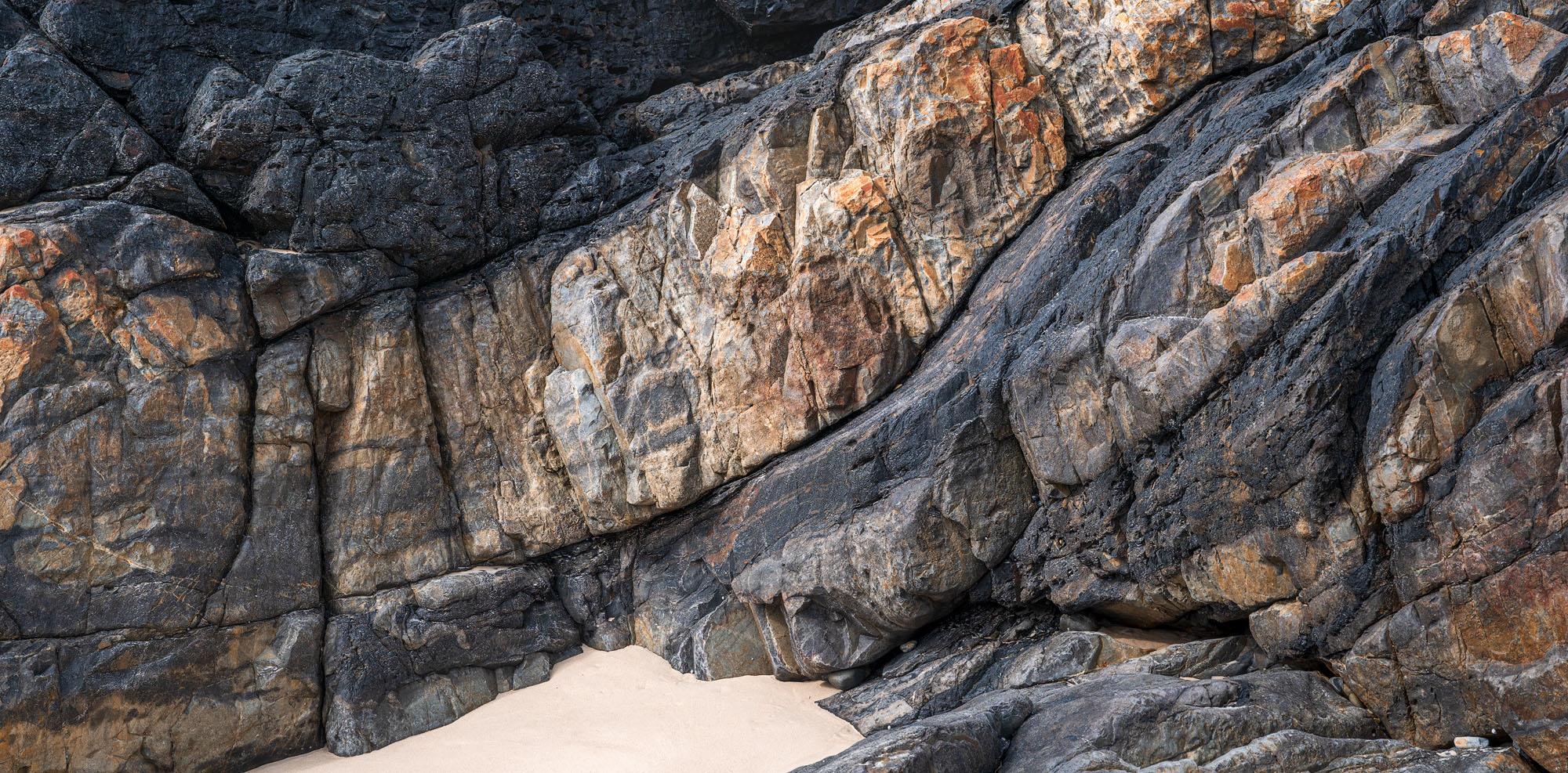 a rockscape showing various textures of the rocks. Not close up. The rocks curve down as if flowing. Layout is black stripe on top, orange-yellow-beige stripe in the middle, black and orange stripe at the bottom.