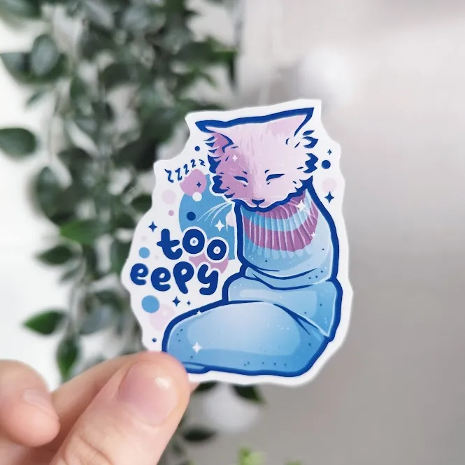 hand holding up a sticker of a kitten sleeping in a sock titled "too eepy"