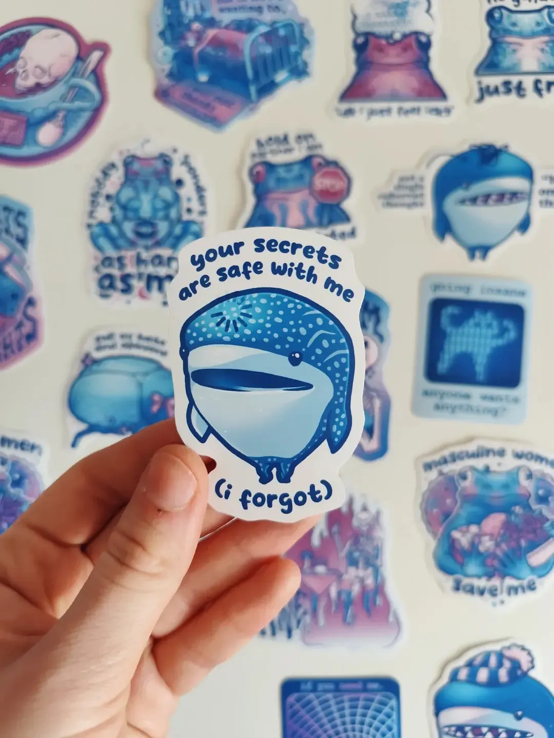hand holding up a sticker of a whale shark titled "your secrets are safe with me (i forgot)"