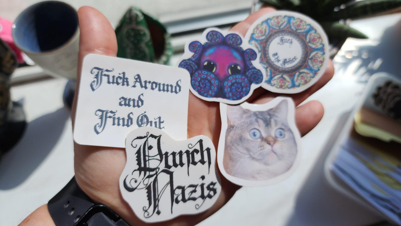 Several hand-cut glossy stickers in a variety of styles on my hand.