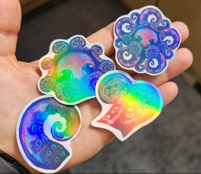Four rainbow-holographic octopus design stickers on my hand.
