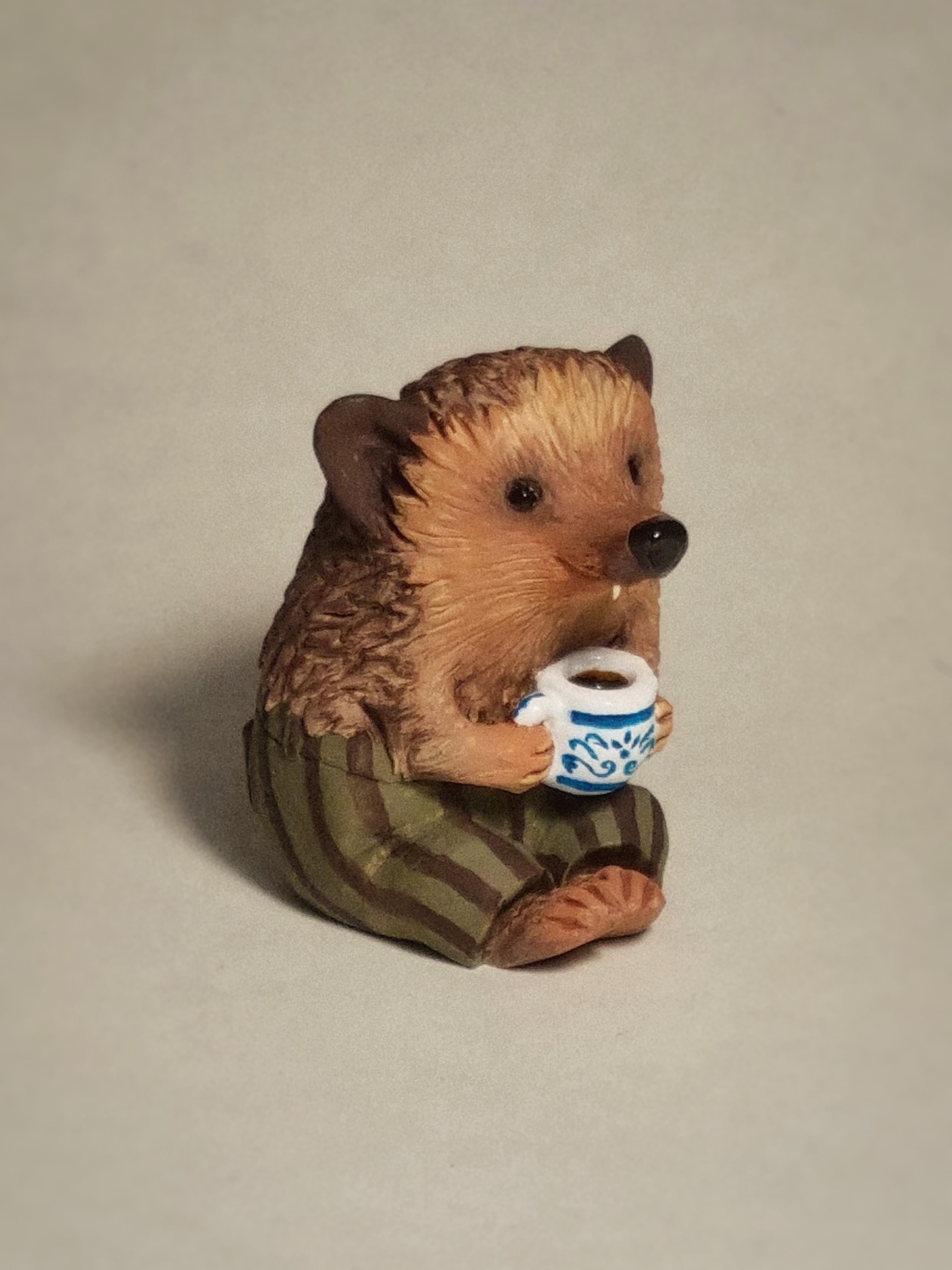 Polymer clay sculpture of a hedgehog with a mug and striped trousers.