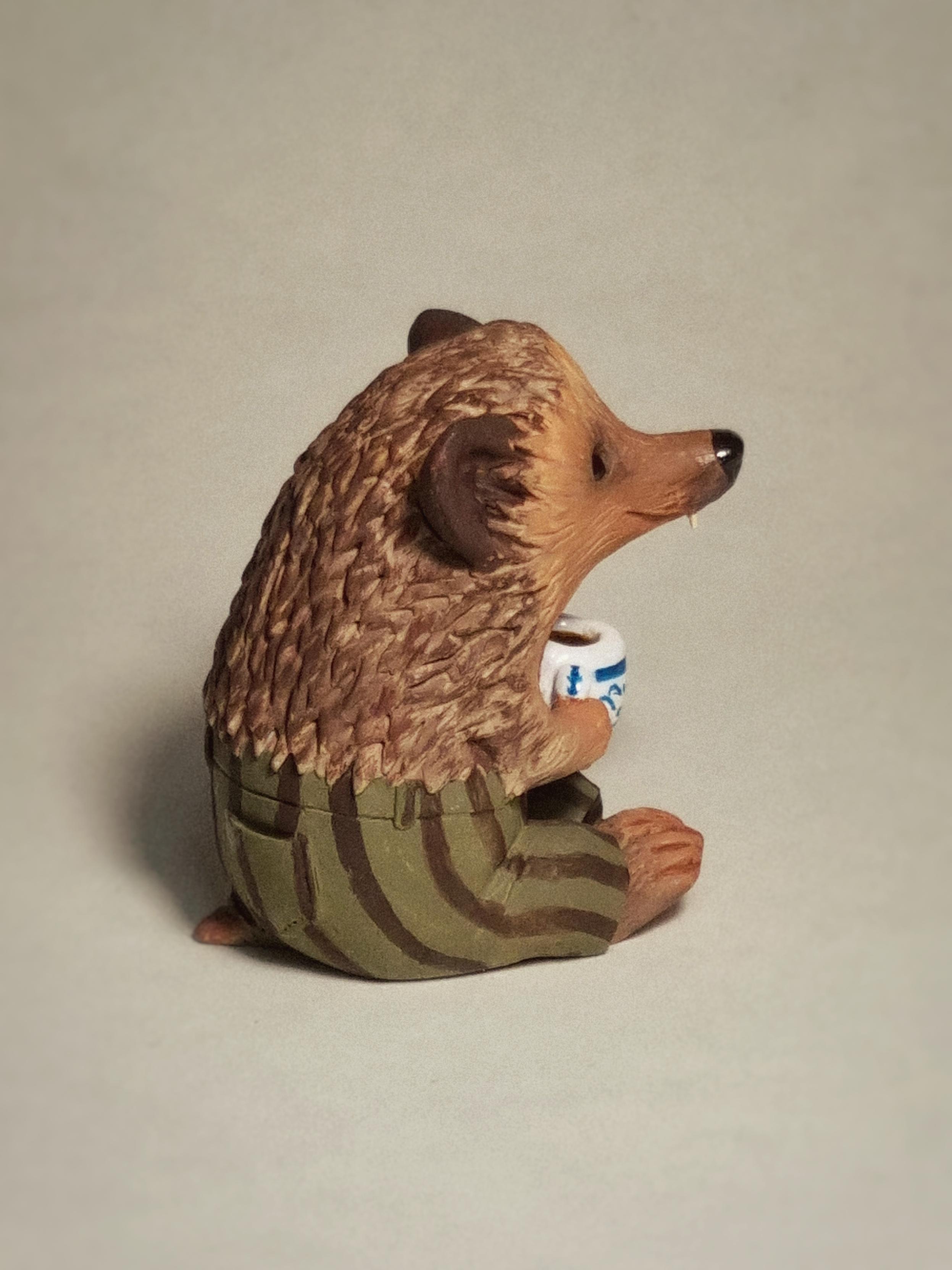 Polymer clay sculpture of a hedgehog with a mug and striped trousers.