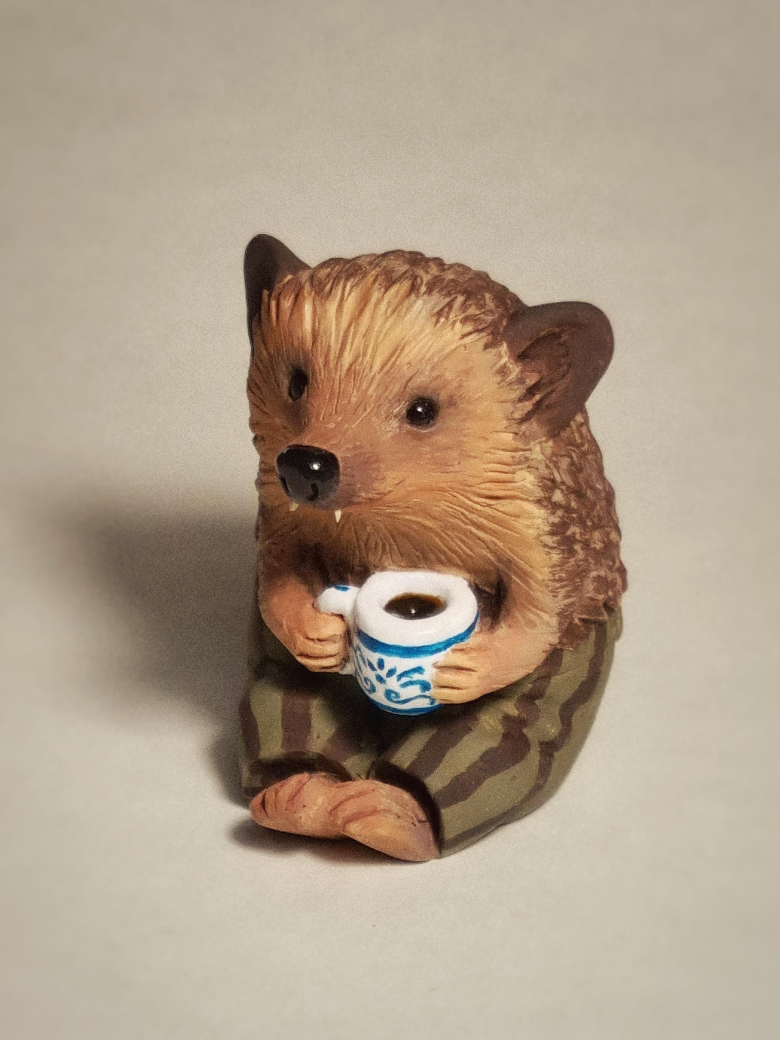 Polymer clay sculpture of a hedgehog with a mug and striped trousers.