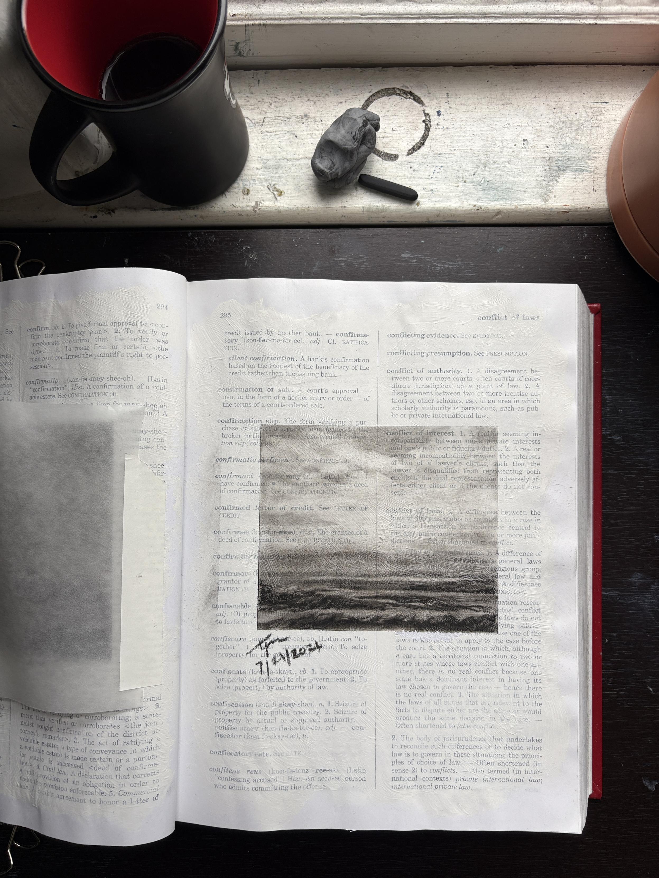 Page 295 in Tisha Mark’s law dictionary. Photo of my law dictionary opened to a page with a charcoal sketch of the sea. Words on the page are partially visible underneath a thin layer of gesso and sketch. On the windowsill at the top of the photo is a coffee cup, piece of charcoal, and a kneadable eraser.