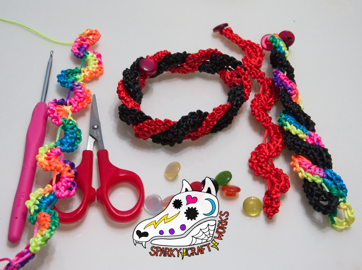 A photo of various wavey-patterned crocheted bracelets and crochet equipment, on top of a grey-white background. To the left is a crocheting needle, next to a rainbow colored bracelet and corcheting scissors. In the middle is a black bracelet and red bracelet, intertwined and held together with two red buttons. Under the bracelets are a collection of varyingly-colored buttons. To the right, is a red bracelet on its own that’s next to a rainbow bracelet and black bracelet intertwined. In the middle and down is the Sparky Craft Works watermark, a stylized calavera-painted wolf skull design.