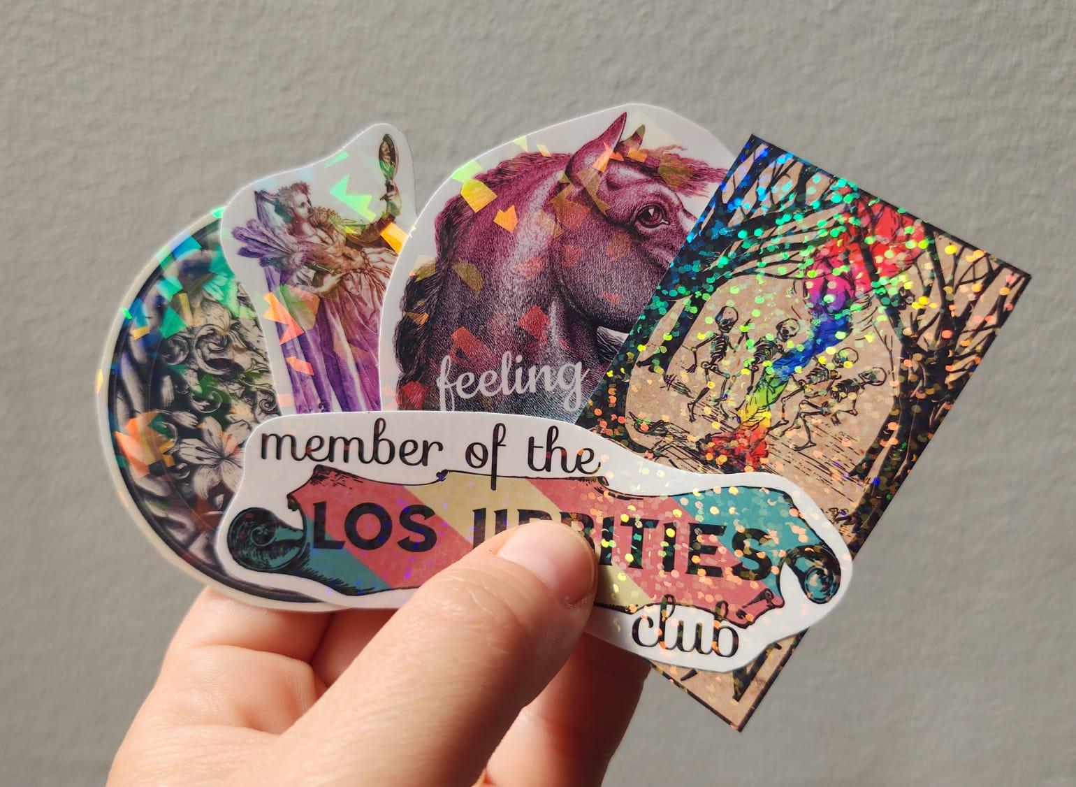 My hand holding up five different colourful holographic stickers