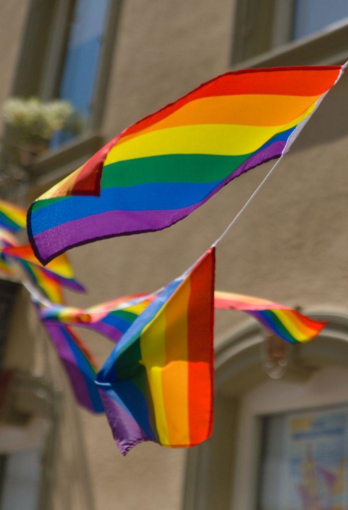 A chain of small Rainbow Flags in a Line hung from the balcony of a historical building. Gently waving in the Wind