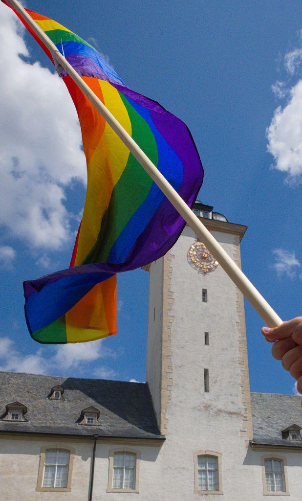 A Rainbow flag being waved in Front of a historical building (clock Tower). Sky''s Sunny with fluffy clouds