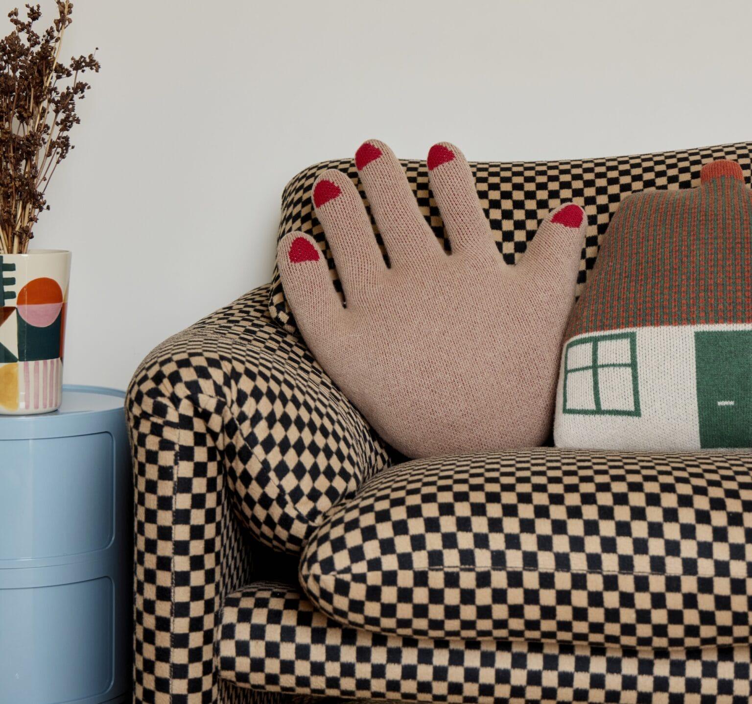 a hand-shaped pillow sits next to a cottage-shaped pillow on a couch with checkered upholstery