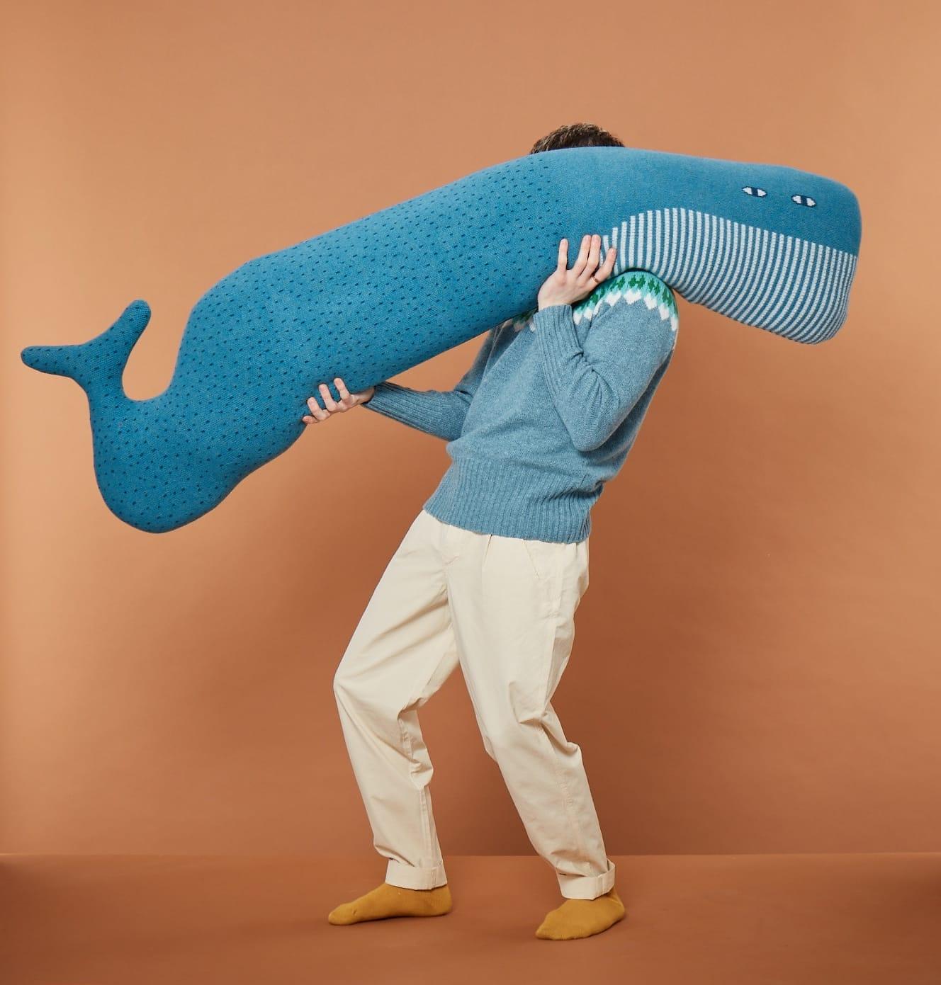 an anonymous male model holds a large whale-shaped bolster pillow over his shoulder