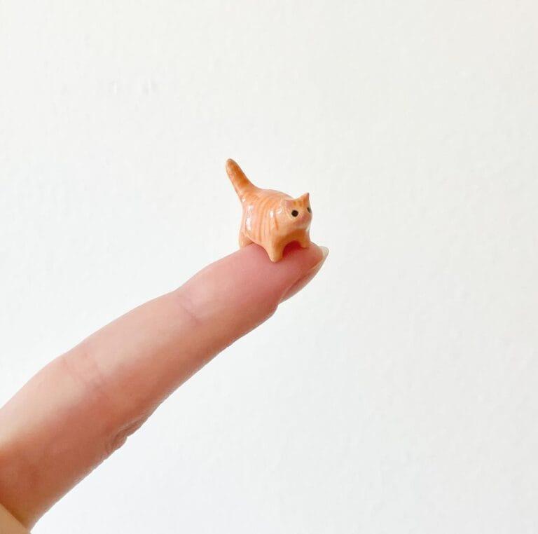 a finger holding a tiny ceramic cat
