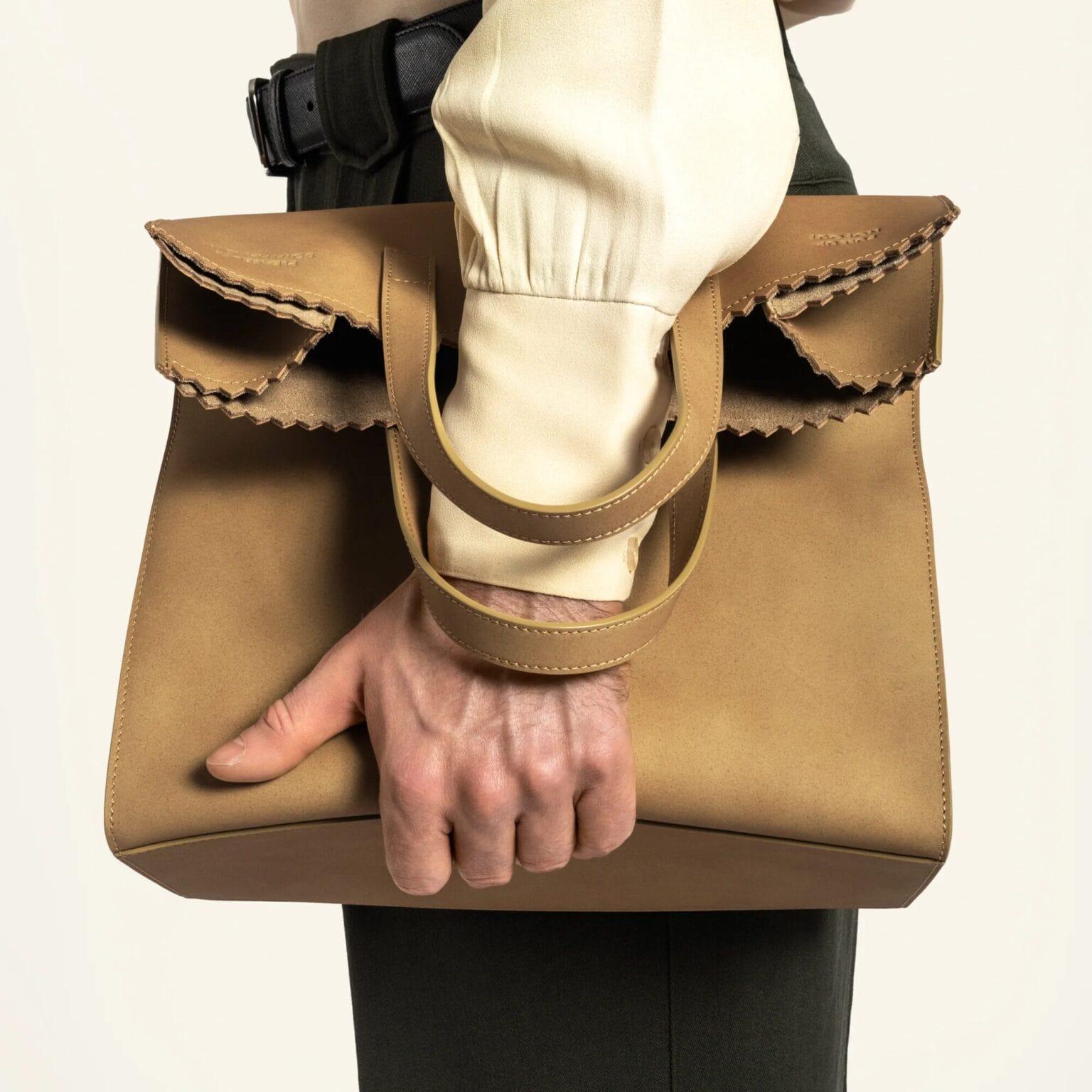 a hand holds a leather tote that looks like a paper bag