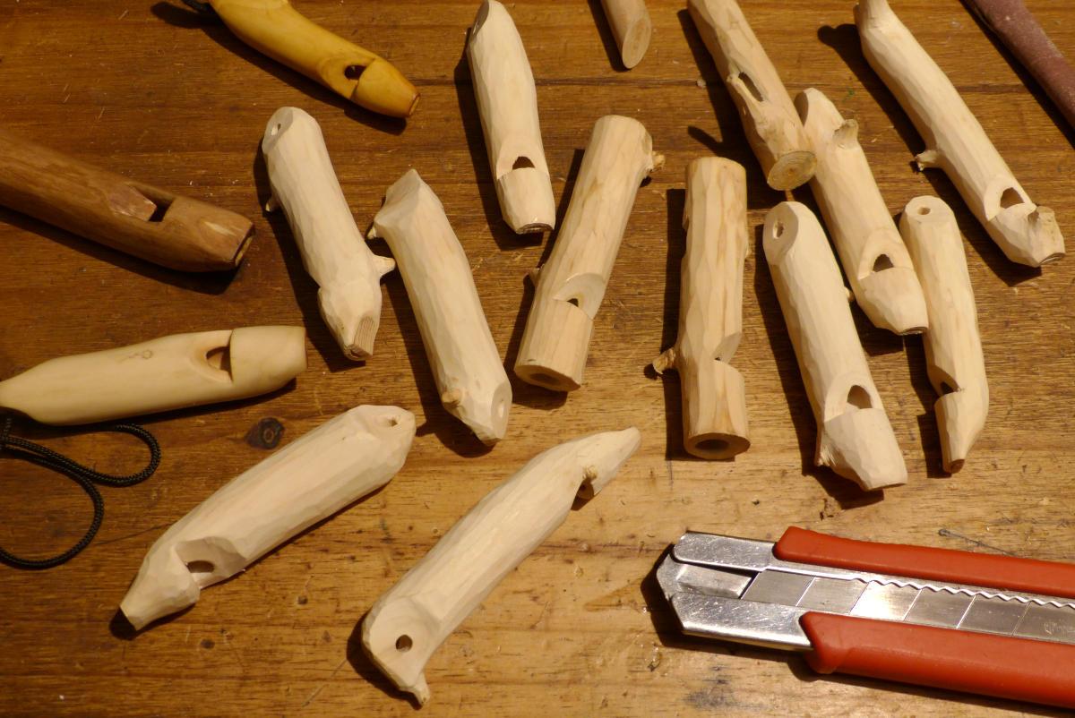 About fifteen unfinished wooden whistles on a table.