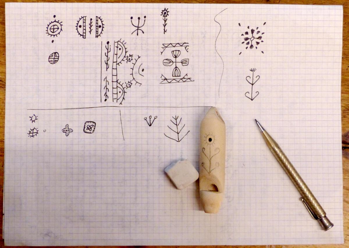 A whistle is placed on a sheet of paper where traditional patterns have been drawn using fine lines.