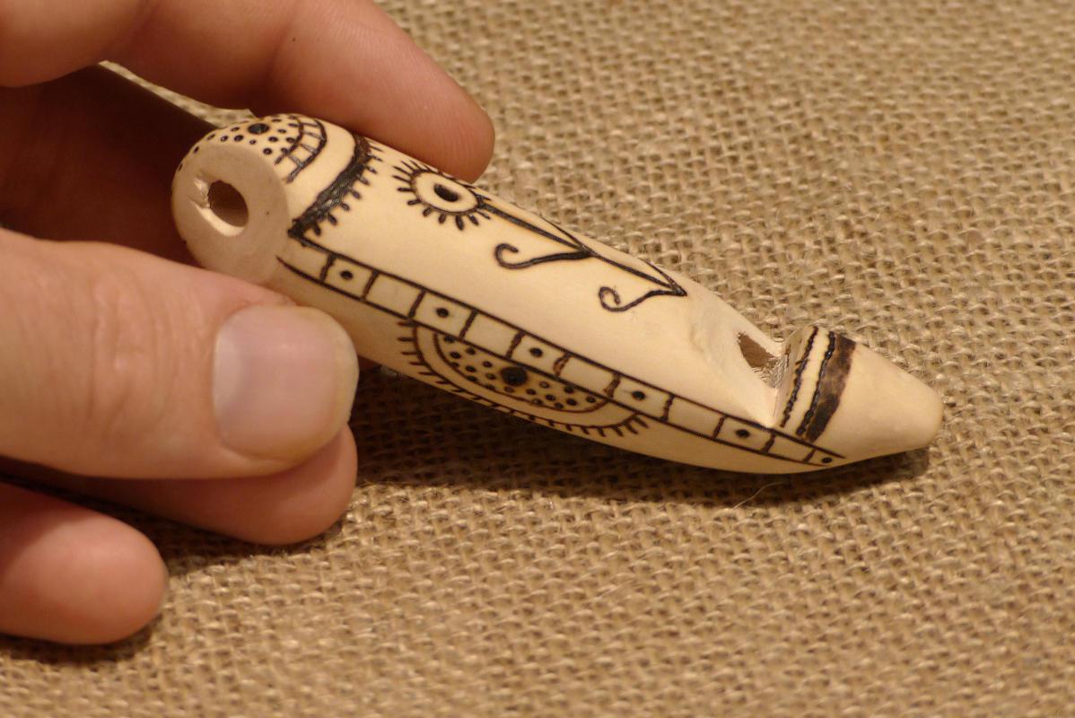 A hand is holding a decorated wooden whistle.