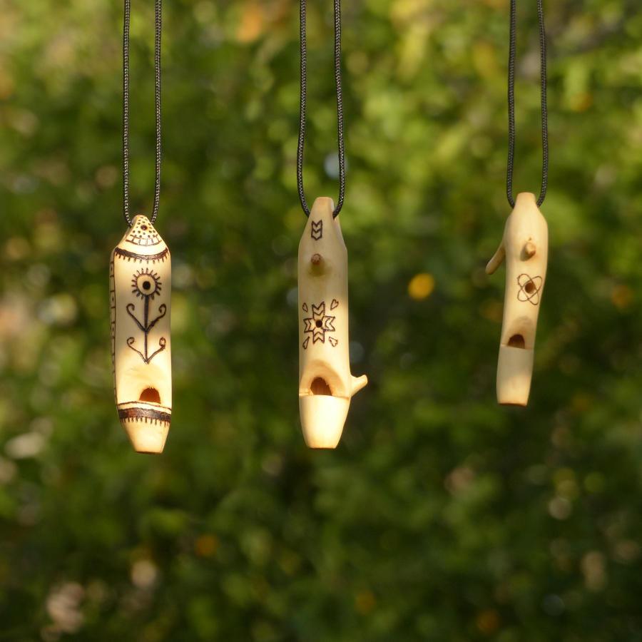 Three whistles hanging in front of some vegetation. All three have a hole and feature traditional pyrographed designs.