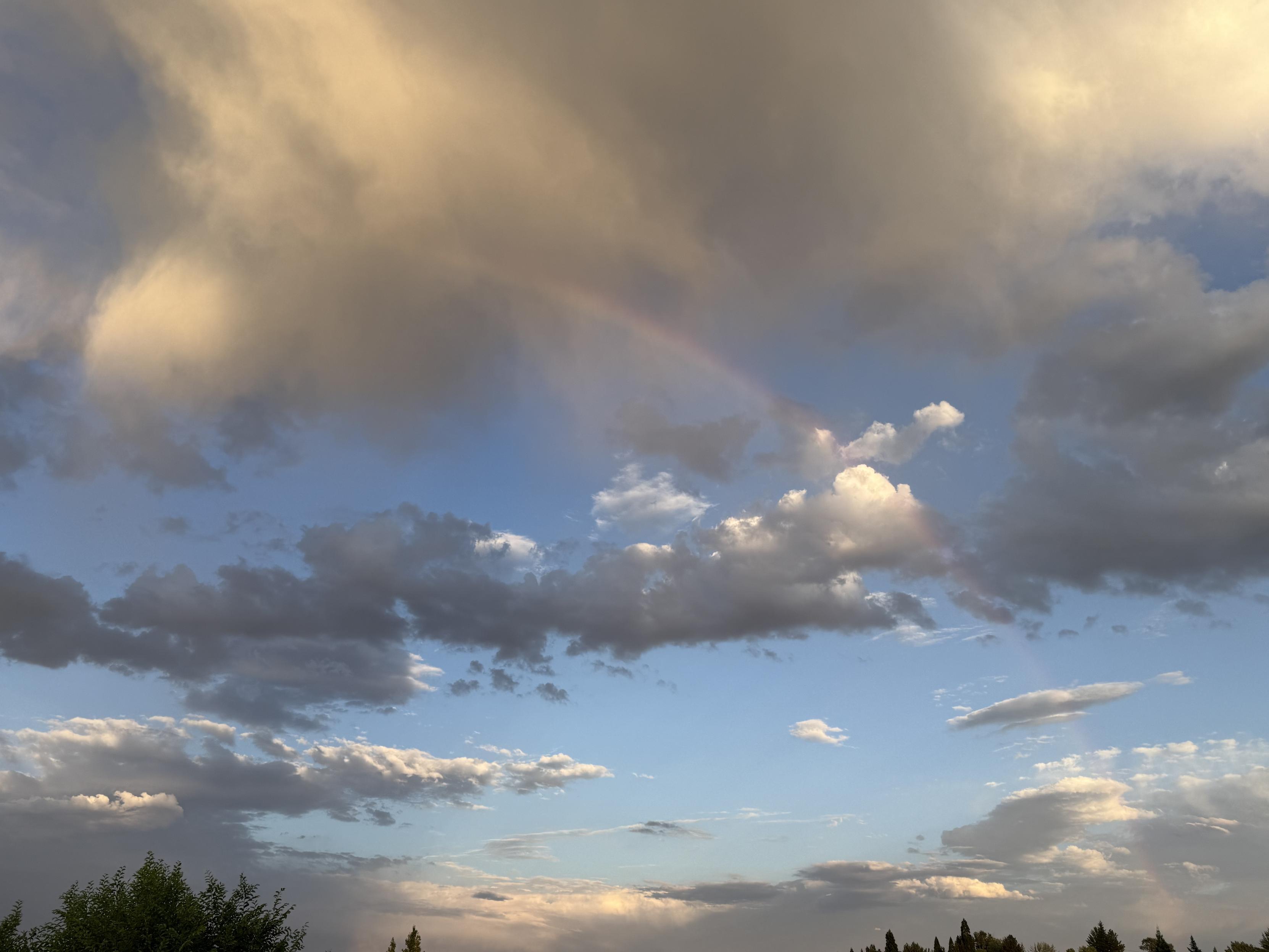 A quarter circle of rainbow, faint, is in the sky that's peppered with clouds.