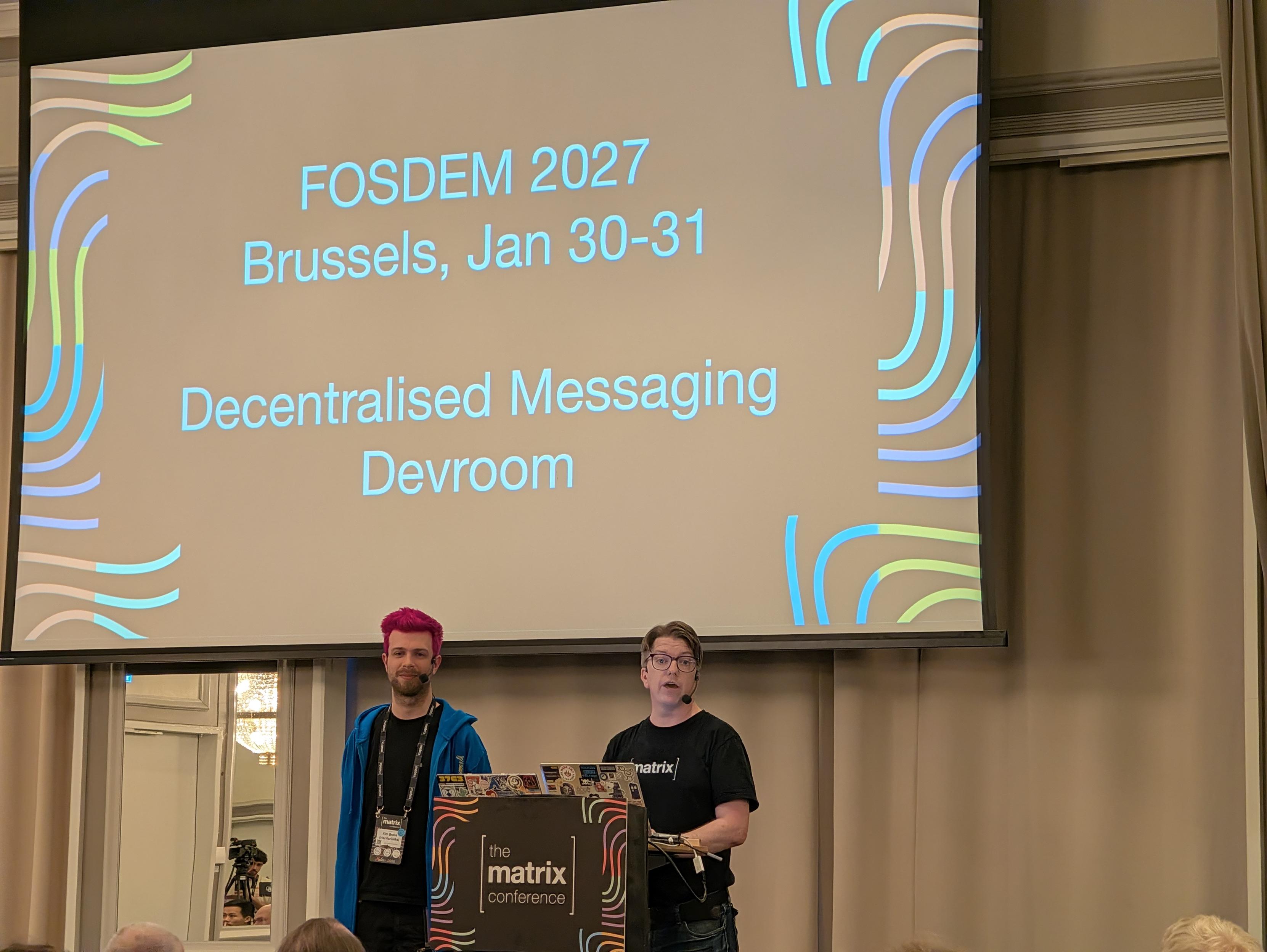 Kim and Andy under a slide saying FOSDEM 2027 Brussels, Jan 30–31 Decentralized Messaging Devroom