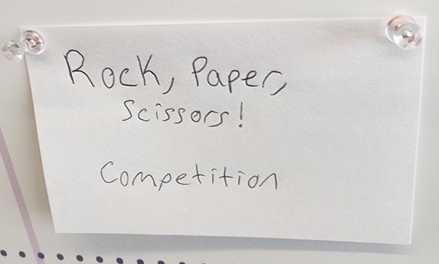 Index card on the open spaces board saying "Rock, Paper, Scissors! Competition"