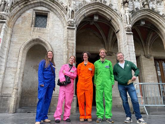 5 people in front of an old building, 4 dressed in colourful boiler suits