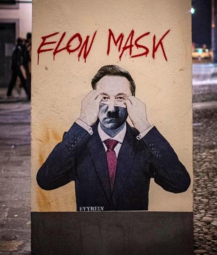 Streetartwall. A mural depicting Elon Musk was sprayed onto a narrow gray concrete wall using stencils. Above the image, "Elon MASK" is written in red lettering and below it, the man in the black suit can be seen pulling a mask off his face. The upper half of his face is Elon Musk, the lower half looks like Adolf Hitler. These kinds of satirical works of art in public spaces in Italy don't usually survive for long. So you should be quick to photograph it.
Info: Evyrein" is a well-known Italian street artist whose art often thrives on contrasts. The seemingly familiar is placed in a new, mostly satirical context. He says: "I want to calm the waves, make people think, shake up their conscience. I want people to pause, if only for a moment, and ask themselves what is happening in the world around them.