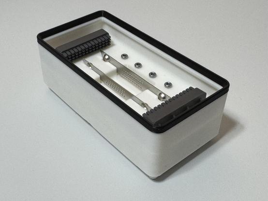 a white 1 x 2 x 4U Gridfinity bin with a black lip around the top.  Designed for and filled with parts from the Bambu lab A1 Mini Heatbed Nozzle Wiper parts box.