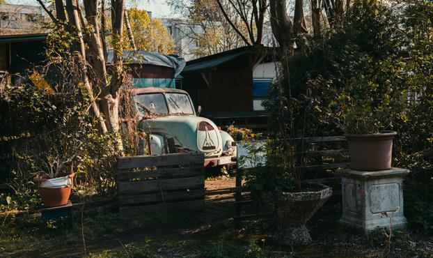 An old car converted into a motorhome. The car is rusty and dirty, yet has a license plate and seems functional