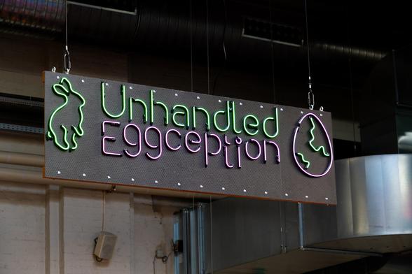 The big neon sign saying "Unhandled Eggception" mounted at the entrance of the venue