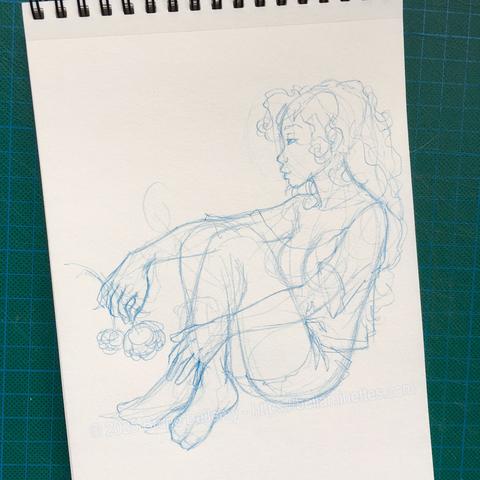 Photo d'un croquis à l'étape de l'ébauche à la mine bleue dans mon carnet à spirale d'une bellaminette aux cheveux longs et assise, vêtue d'un T-shirt et d'un short, le regard rêveur porté vers le lointain. Son bras droit repose nonchalamment sur ses genoux, et dans la main droite elle tient une fleur de pivoine.