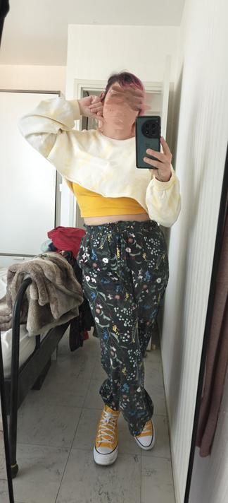 Selfie in a mirror, wearing green flowery pants and yellow crop top under a crop white and yellow long sleeve top and yellow shoes.