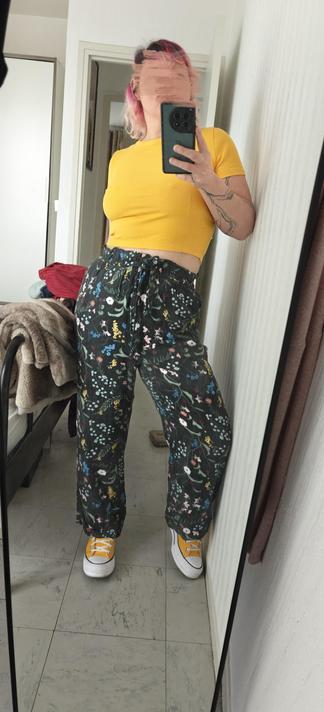 Selfie in a mirror, wearing green flowery pants and yellow crop top and yellow shoes.