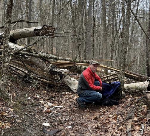 posed with backpack in front of the large downed tree and smaller trees it crushed, completely covering the hiking/biking trail