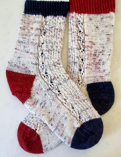 A pair of hand-knitted socks. Body of each sock is speckled hand-dyed yarn, base colour cream. speckles - blue, grey, deep red.
Cuffs, toes & heels - navy, red, navy on one sock; red, navy, red on the other.
There is a lacy cable runniing down the side of each sock