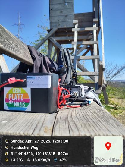 Battery and cables on a bench, a wooden watchtower in the background