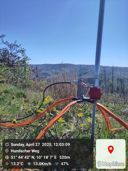 The bottom of a vertical antenna with yellow wires and cable, a mountain view in the background