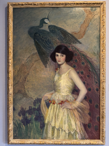 photo of painting #1 gold frame  “The diverse Art Deco style of geometric forms, modern luxury, & bold vibrant color palettes reflected the social & technological progress of the 1920s-30s. Visual artists felt its influence, as modernity impacted nearly every medium. Among these artists was the Long Island-based F. Edwin Church…. Esteemed for his portraits of women that reflected the growing Euro-American interest in Japanese art, he painted a variety of subject matter, including luxurious portraits, displaying versatility in technique. He captured beaming skin tones & ornately textured fabrics, captivating the viewer with dramatic compositions. Throughout the late 1910s-30s, Church painted various women in verdant Japanese-inspired settings. In his Girl in Yellow, c.1920, a slender woman with short dark hair confidently poses in a bright yellow dress that elegantly flows & stands out to the viewer in a composition inspired by the Japanese master Hiroshige.” Bird behind woman: Peacock