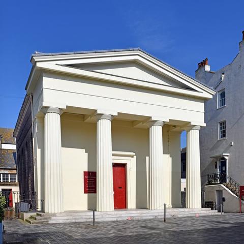 Photo of a Unitarian church designed by Amon Henry Wilds for John Chatfield, 1820, in Greek Revival style. Stucco over brick, four fluted Doric columns portico.  Grade 2 listed. New Road, City of Brighton & Hove, UK.