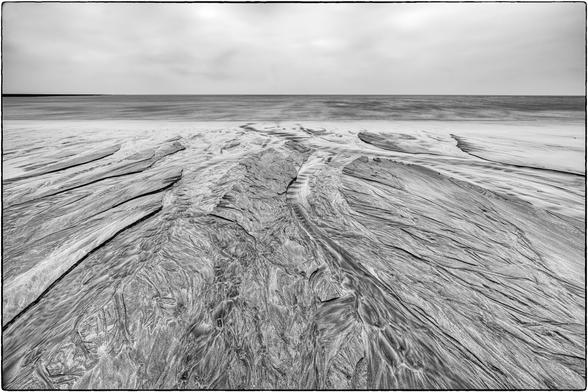 Schwarzweissfotografie mit Langzeitbelichtung am Sandstrand mit durch Gezeiten entstandenen Texturen.