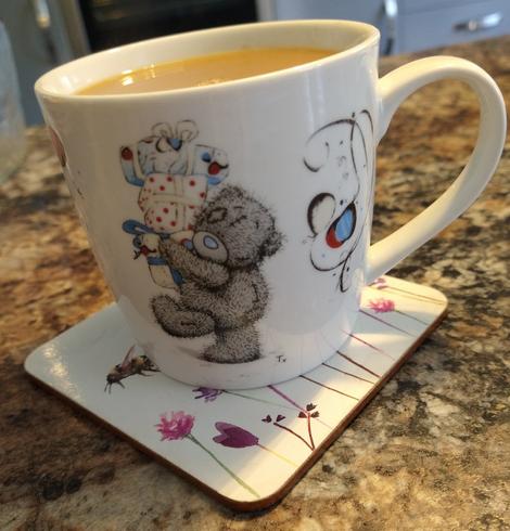 Small mug of tea on a kitchen countertop, with a tatty teddy carrying gifts