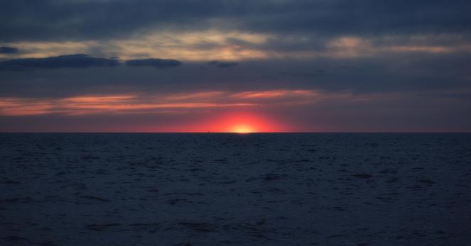 A captivating sunset casts vibrant hues across the horizon, with the sky gradually transitioning from a deep blue to a soft orange glow. The gentle waves of the ocean blend seamlessly into the serene scene, creating a tranquil ambiance.