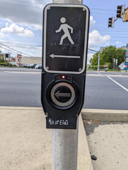 A pedestrian cross walk signal button, with "Kill Ur Ego" handwritten in angular silver letters beneath.