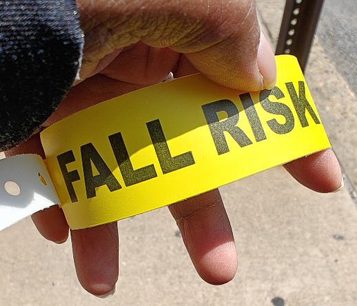 a brown hand holding a bright yellow band with Fall Risk written in black all caps