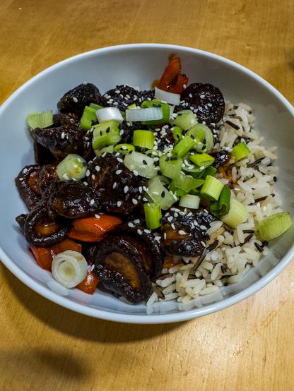 Knusprige Shiitakepilze in süßscharfer Sauce auf Reis, mit Frühlingszwiebeln, in einer weißen Schüssel
