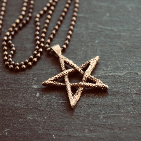 A close-up of the vintage pentagram pendant necklace described in the previous photo on a dark grey slate background. The mottled/rough surface of the pentagram is noticeable.