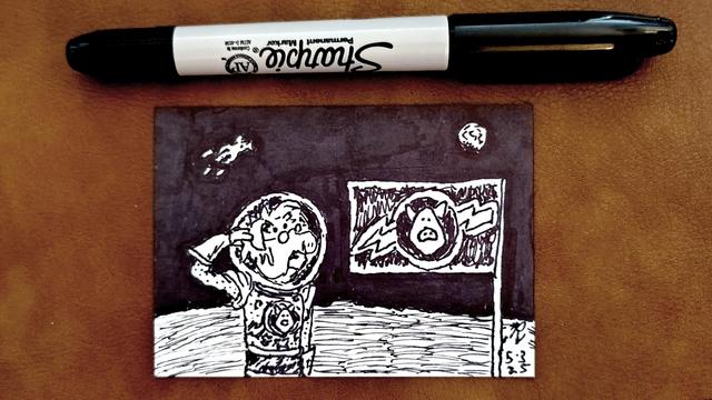 Marker drawing on an artist trading card of Dr. Julius Strangepork from the "Pigs In Space" segment of "The Muppet Show." The image is a spoof of the famous photos of Neil Armstrong saluting a US flag placed on the moon; in this version it's Strangepork saluting a flag of the "Pigs In Space" logo on the lunar surface while the Earth and the U.S.S. SwineTrek are visible in the sky. The drawing is signed with my "RV" signature glyph and dated 5-3-25. The double-tipped black Sharpie marker used to draw the image rests on the table above the card.