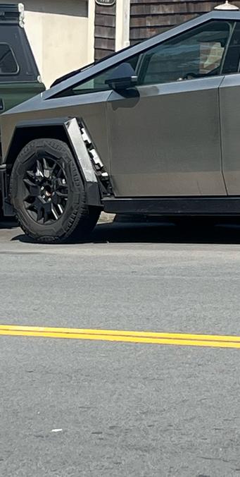 A picture of a cybertruck with part of the front wheel well falling off